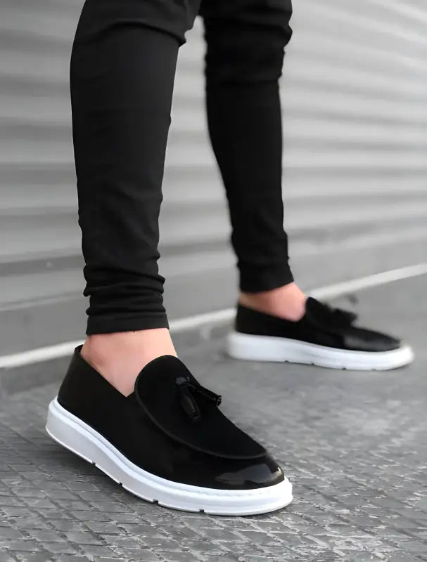 Black suede loafers with white soles and decorative tassels.