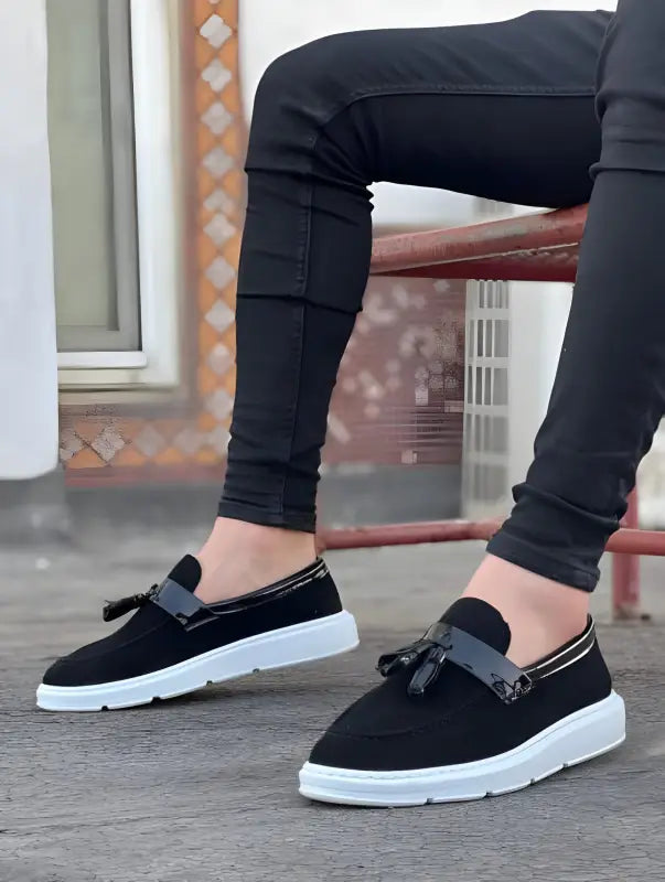 Black suede loafers with white soles and decorative tassels.