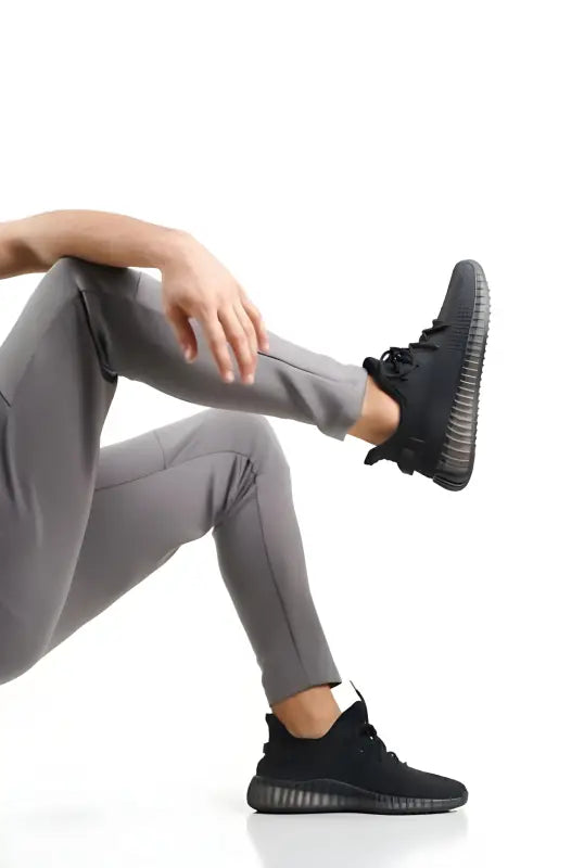 Black athletic sneaker with a textured rubber sole worn with gray leggings.