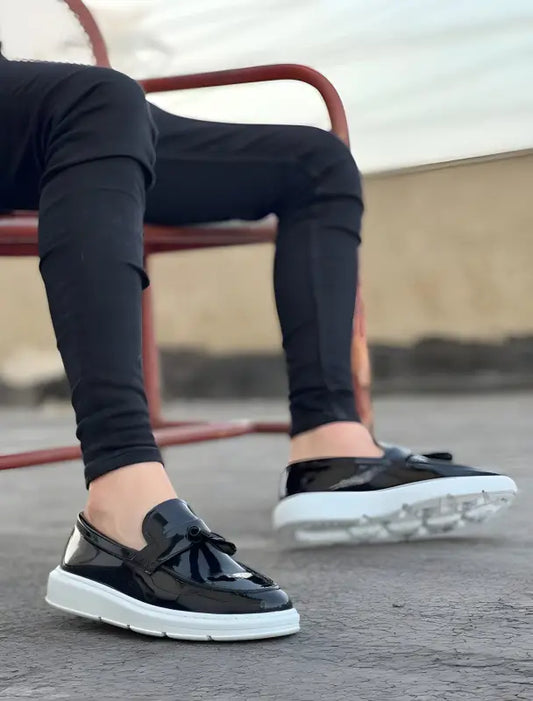 Black leather loafers with white soles and laces worn with dark pants.