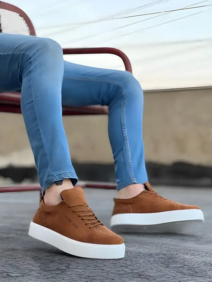 Brown leather sneakers with white soles paired with blue jeans.