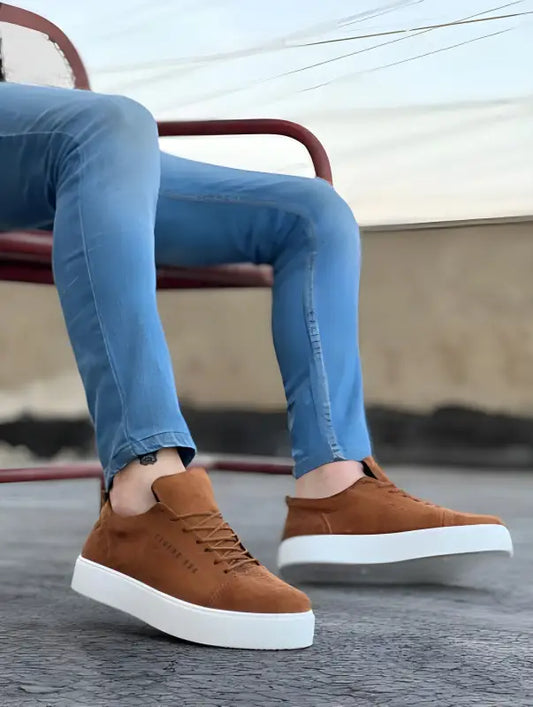 Brown leather sneakers with white soles paired with blue jeans.