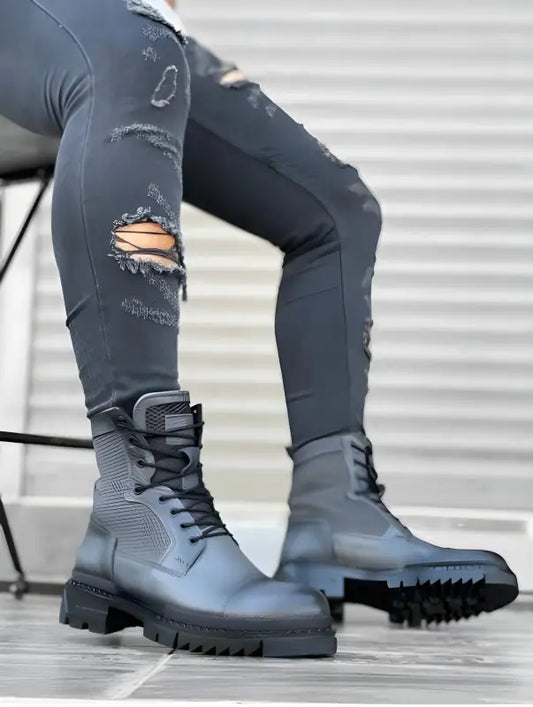 Grey combat boots with thick treaded soles paired with distressed denim jeans.