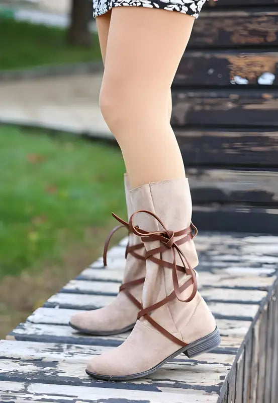 Beige suede knee-high boot with brown leather wrap-around laces.