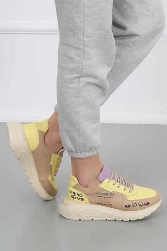 Yellow and beige chunky sneaker with handwritten-style text details and a thick platform sole.