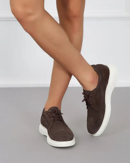 Brown suede sneakers with white soles and laces on feet.