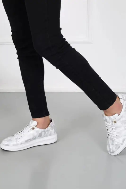 White leather sneakers with metallic silver accents paired with black pants.