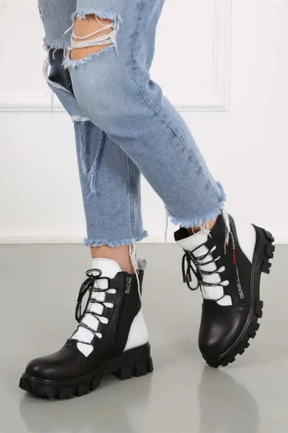 Black and white combat boots with chunky soles and contrasting laces worn with ripped jeans.