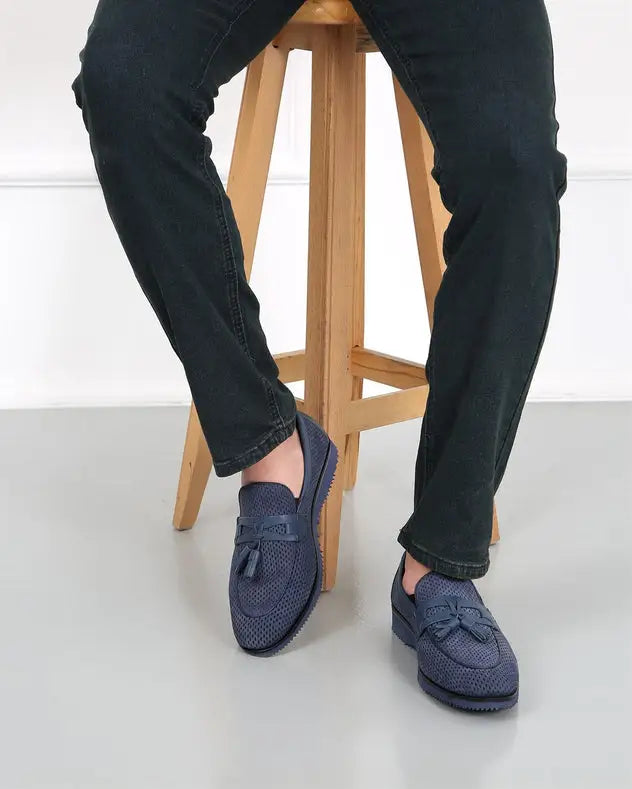 Navy blue suede loafers with tassels worn with black pants.