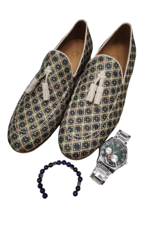 Patterned loafers with white tassels alongside a bracelet and wristwatch.