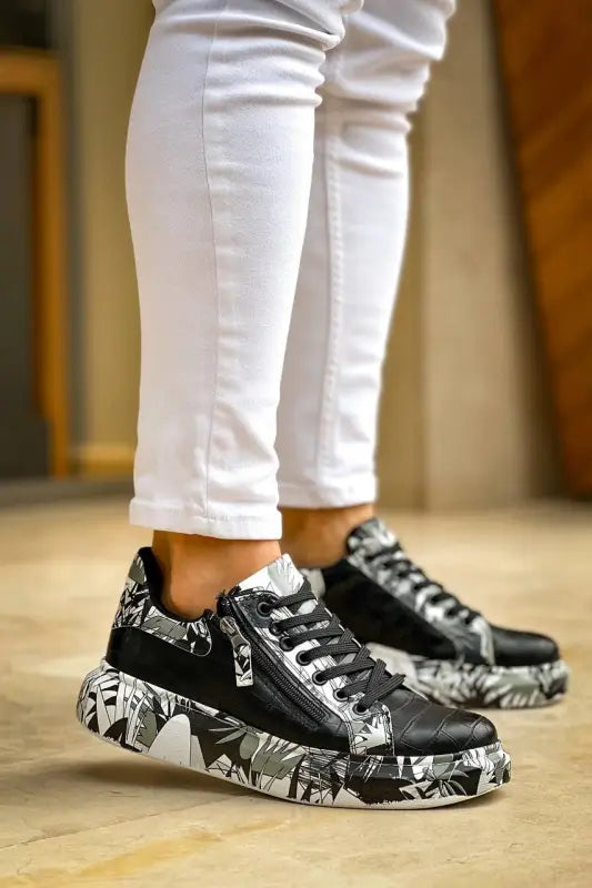 Black sneakers with comic-style graphic print on the platform sole, paired with white pants.