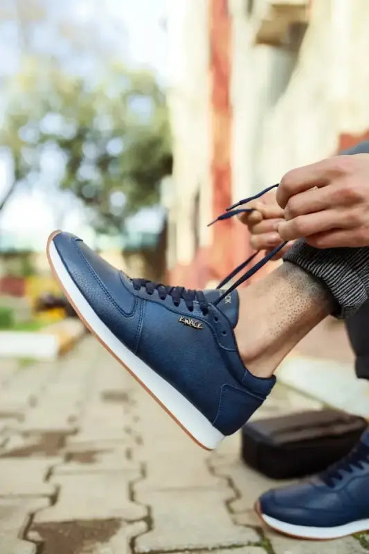 Navy blue leather sneaker with white sole and laces being tied.