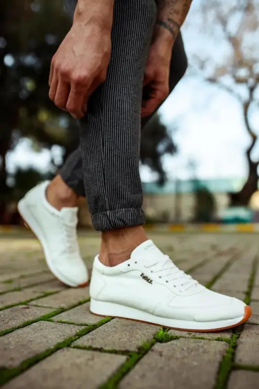 Clean white sneakers with orange-accented soles paired with pinstriped pants.