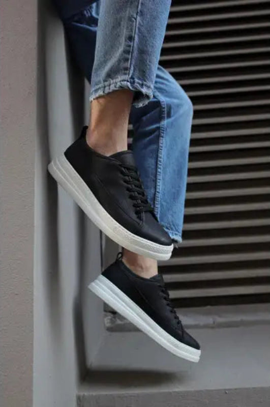 Black leather sneakers with white soles paired with blue jeans.