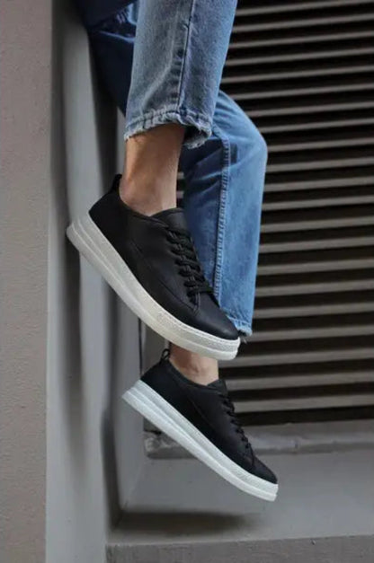 Black leather sneakers with white soles paired with blue jeans.