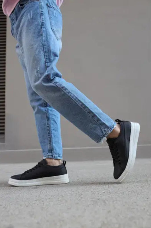 Black sneaker with a white sole paired with distressed light-wash jeans.