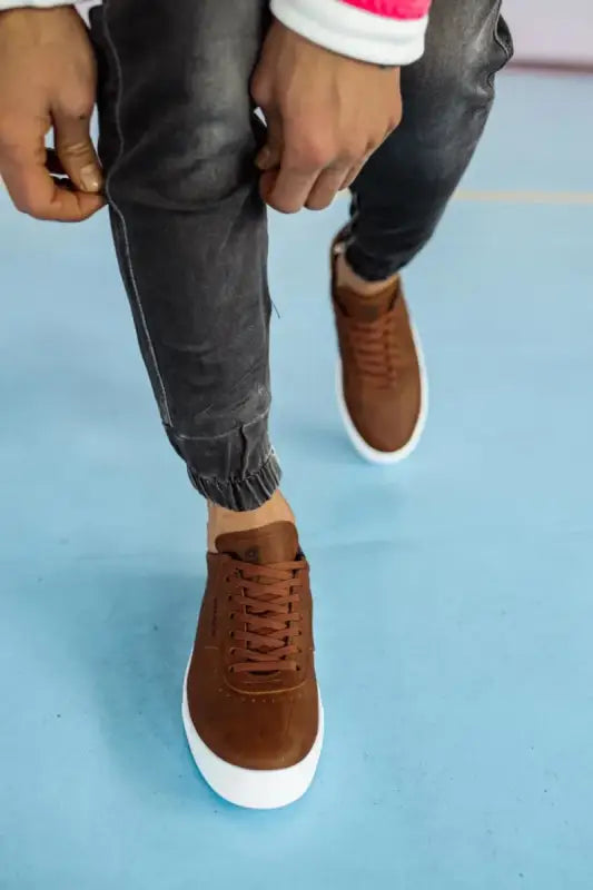 Brown suede sneakers with white soles and dark gray pants.