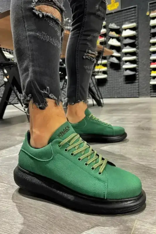 Green sneakers with thick black soles and yellow laces.