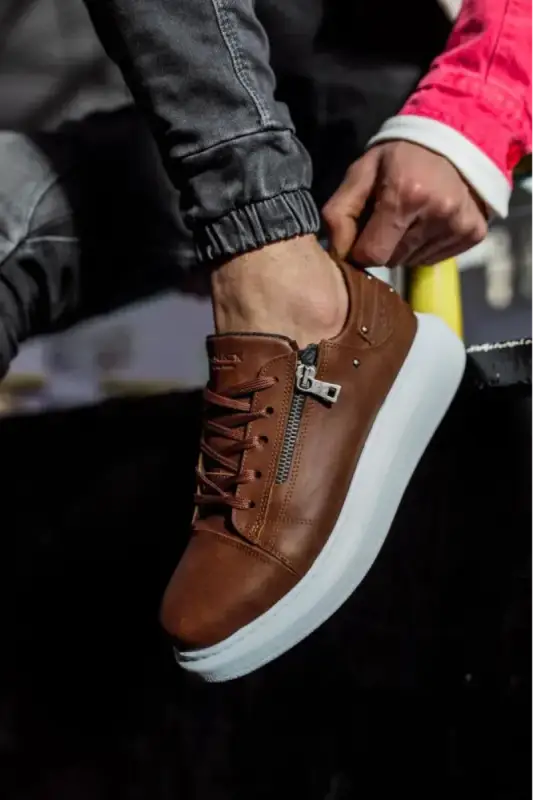 Brown leather sneaker with white sole and side zipper detail.