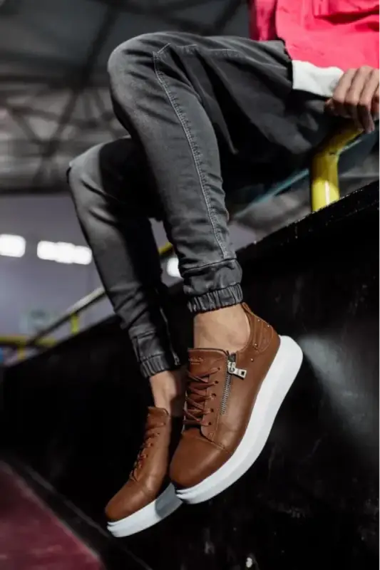 Brown leather sneakers with white soles and black laces worn with dark jogger pants.