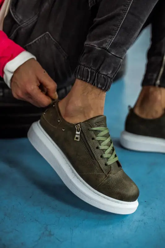 Olive green sneaker with white sole and side zipper detail.