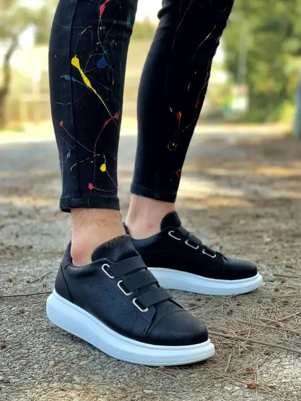 Black sneakers with white soles and elastic laces.