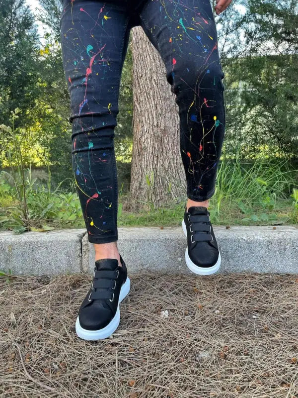 Paint-splattered dark jeans with black sneakers.