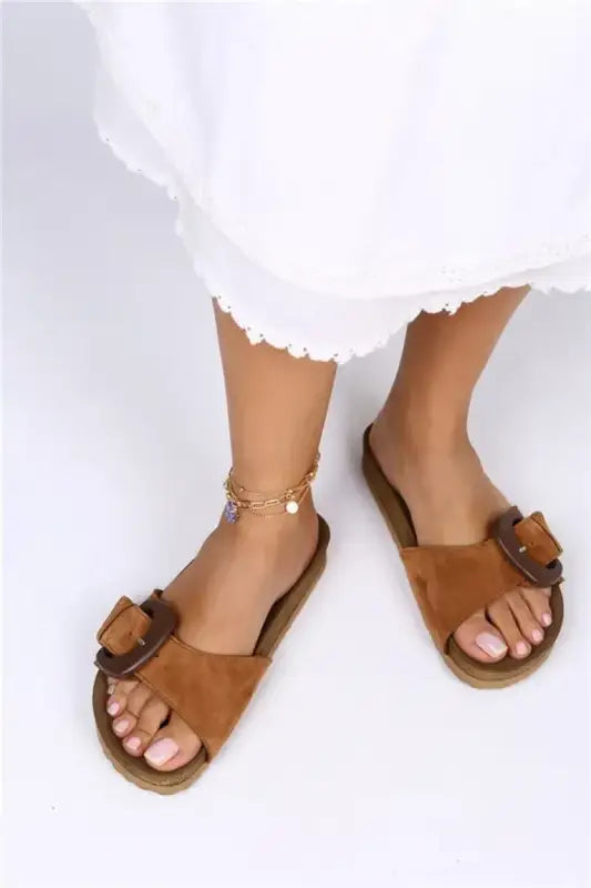 Brown leather sandals with decorative bow details and a delicate ankle chain.