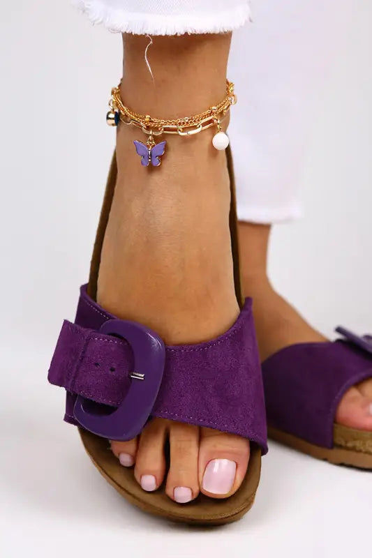 Purple suede sandal with a decorative buckle and a gold ankle bracelet with butterfly charm.