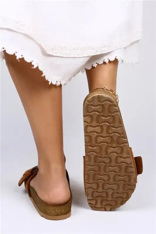 Brown suede sandal with a textured sole and bow detail.