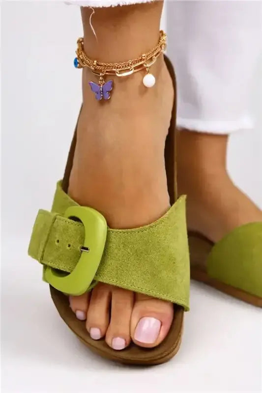 Lime green suede sandal with a prominent buckle and an ankle chain featuring butterfly and pearl charms.