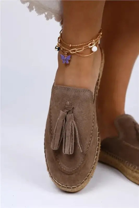 Taupe suede loafer with decorative tassels and a flat espadrille sole.