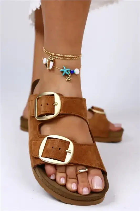 Brown leather sandal with double buckle straps and a gold ankle bracelet.