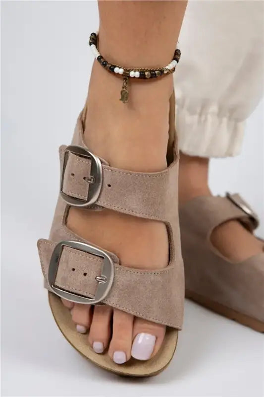 Beige suede sandal with two buckle straps and a beaded ankle bracelet.