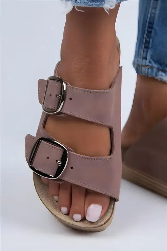 Pink leather double-buckle sandal with white-painted toenails visible.