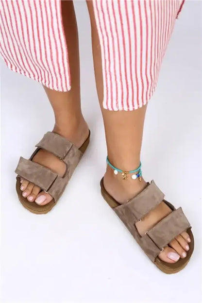 Brown suede Birkenstock-style sandals with two straps worn with striped pants and an anklet.