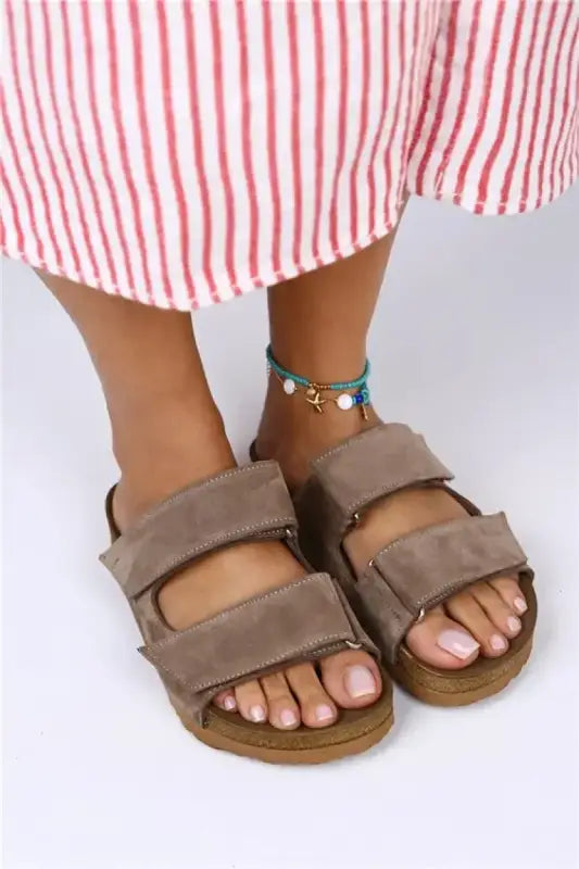 Brown leather Birkenstock-style sandals with two adjustable straps worn with an anklet.