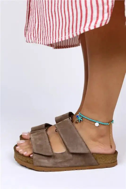 Brown suede Birkenstock-style sandal with two adjustable straps worn with a turquoise anklet.