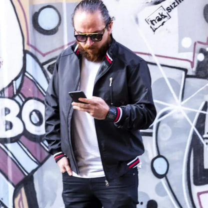 A bearded person wearing sunglasses and a black jacket checking their phone.