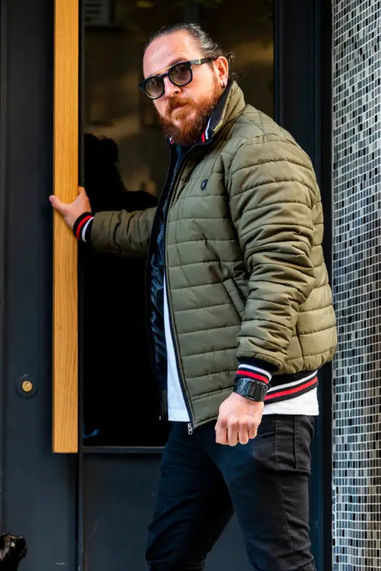 A bearded person wearing a khaki puffer jacket and sunglasses.