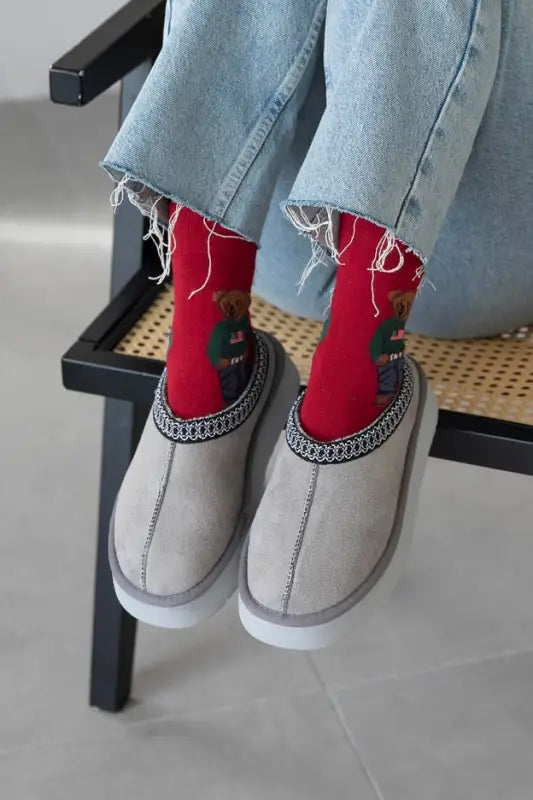 Person wearing red socks with teddy bear design and gray slippers.