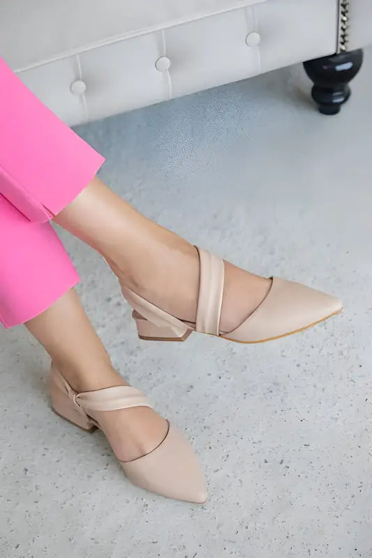 Nude-colored pointed-toe flats with asymmetrical straps across the foot.