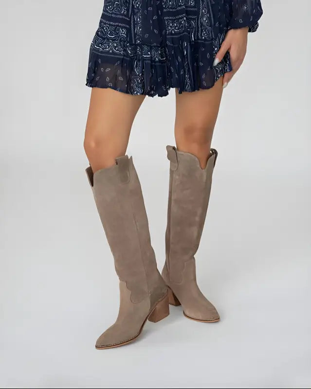 Tall taupe suede cowboy boots with pointed toes and stacked heels.