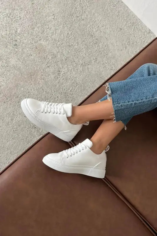 White leather sneakers with laces paired with light blue denim jeans.