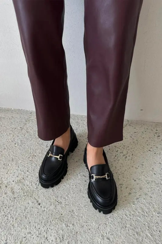 Black leather horsebit loafers paired with burgundy trousers.