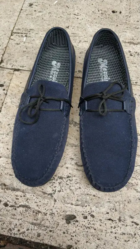 Navy blue suede driving loafers with decorative laces on top.